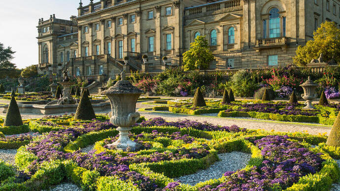 A formal garden with statues and low hedges in front of a stately house