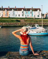 Woman sitting on the wall of a harbour looking at the boats
