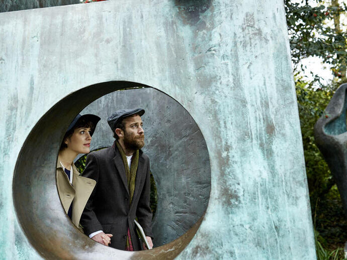 Couple seen through a gap in a large bronze sculpture in a garden