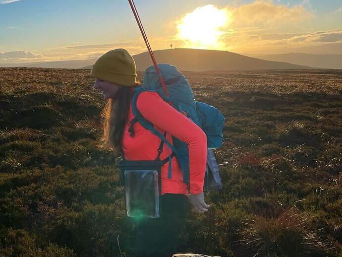 Female hiker with a backpack and walking poles, hiking through the countryside of Kilder in Northumberland at sunrise