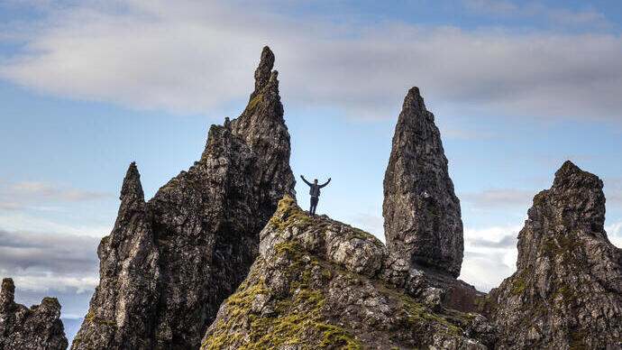 Man standing at basalt pinnacles, arms outspread