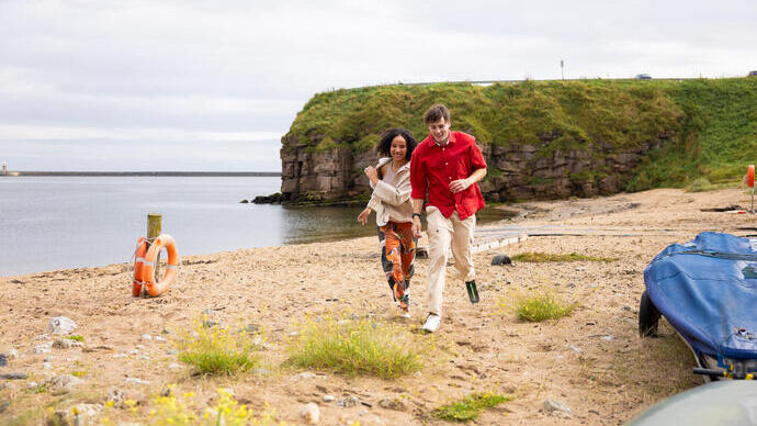 Two friends race along the beach near Tynemouth.