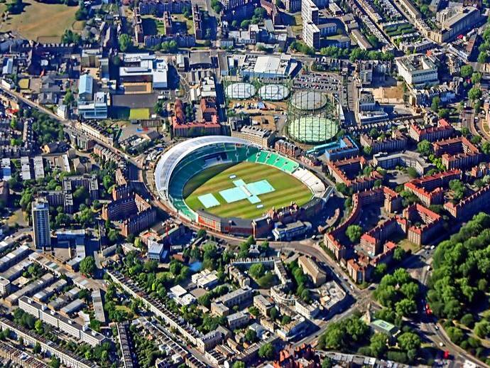 Aerial view scanning over city with large cricket ground, parks and buildings