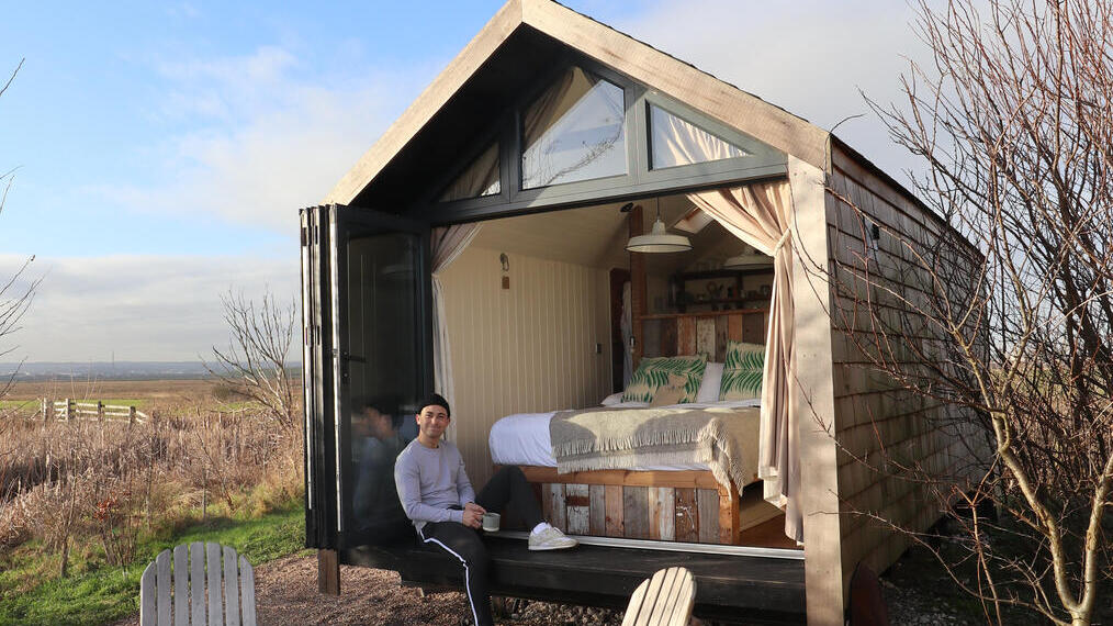 Mann, der am Eingang einer Hütte in einer Landschaft sitzt