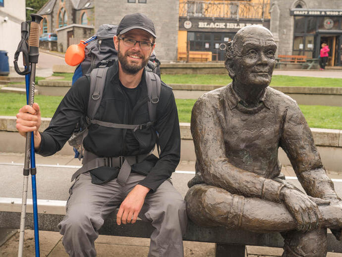 Un homme avec des cannes posant à côté d'une statue sur un banc à Glasgow