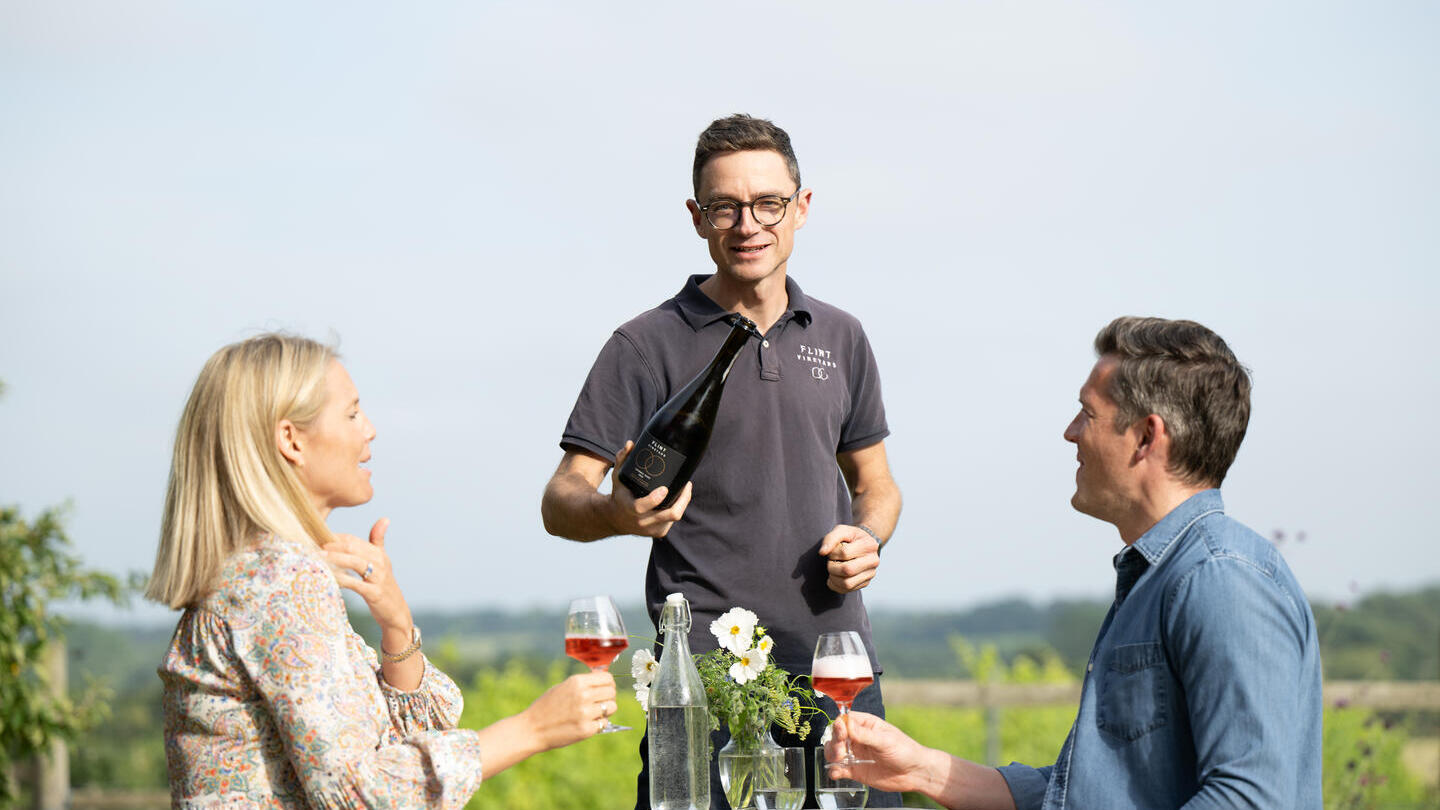 A waitor serving wine to a couple in a vineyard