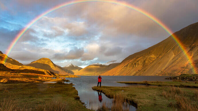 Man standing on the edge of a lake watching a rainbow