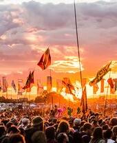 Glastonbury Festival, showing crowd of people at sunset with flags waving
