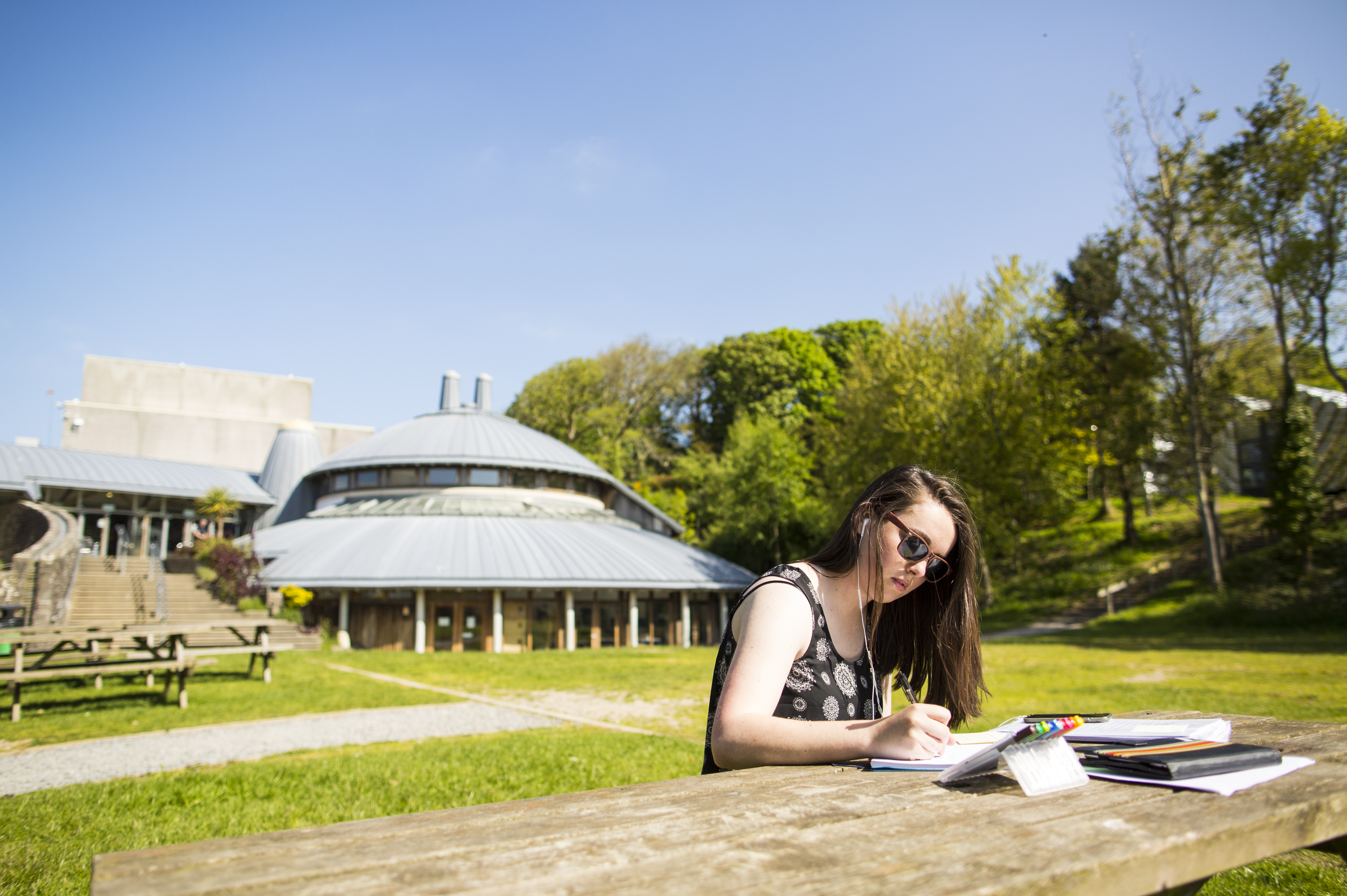 A person sitting at a bench writing outside Aberystwyth Arts Centre