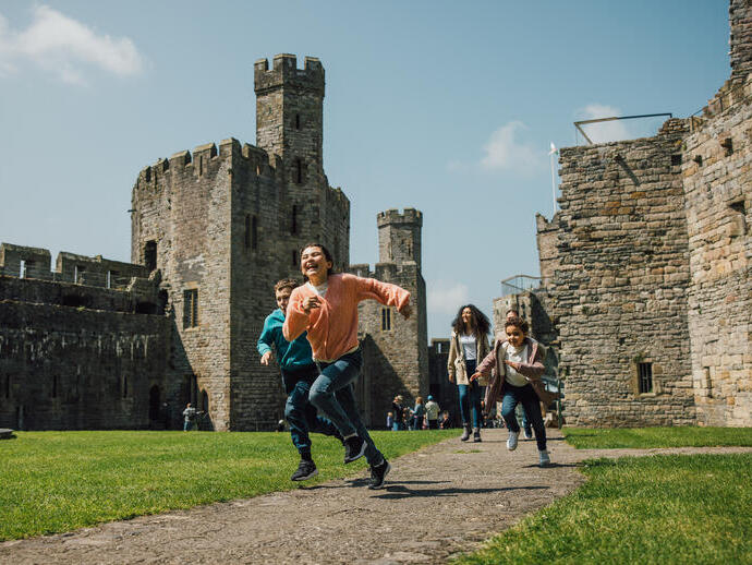 Bambini che corrono e ridono presso un castello di pietra storico in una giornata di sole.