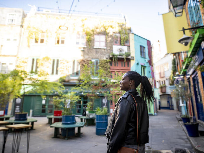Female tourist exploring a London shopping courtyard with shops and outdoor seating.