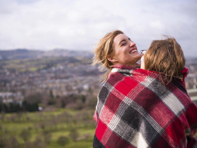 Two women wrapped in red checkered blanket standing on a hill overlooking a city