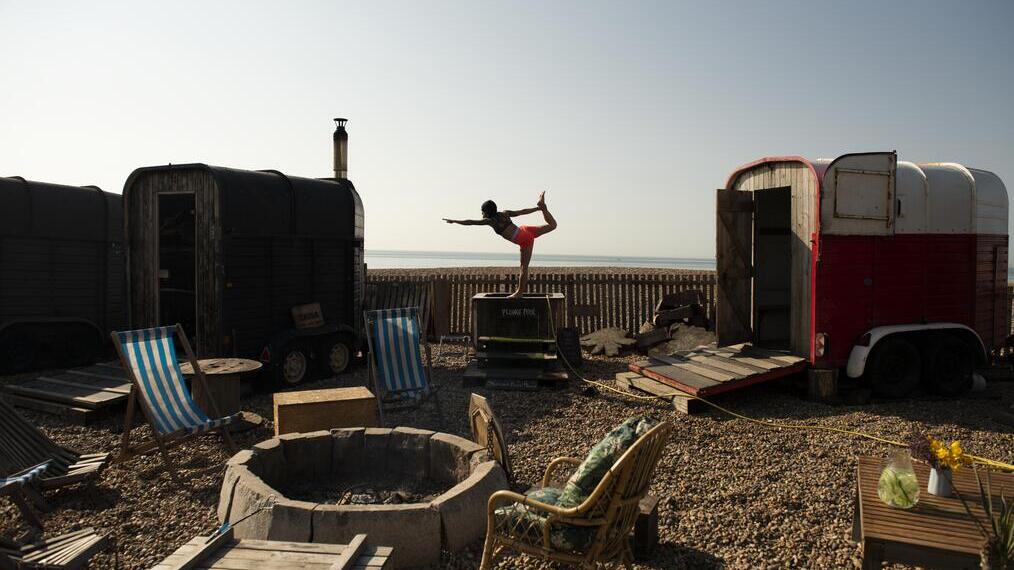 Woman holds a yoga pose standing on the edge of small plunge pool on the beach