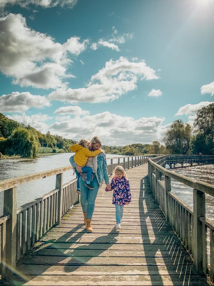 Familie überquert bei Sonnenschein einen Holzsteg über den Fluss