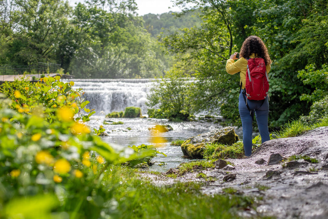 A woman stand by a waterfall and takes a picture