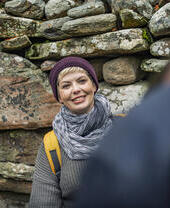 Woman wearing hat and scarf posing in front of a stone wall