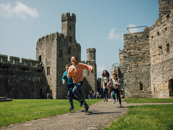 Children running and laughing at a historic stone castle on a sunny day.