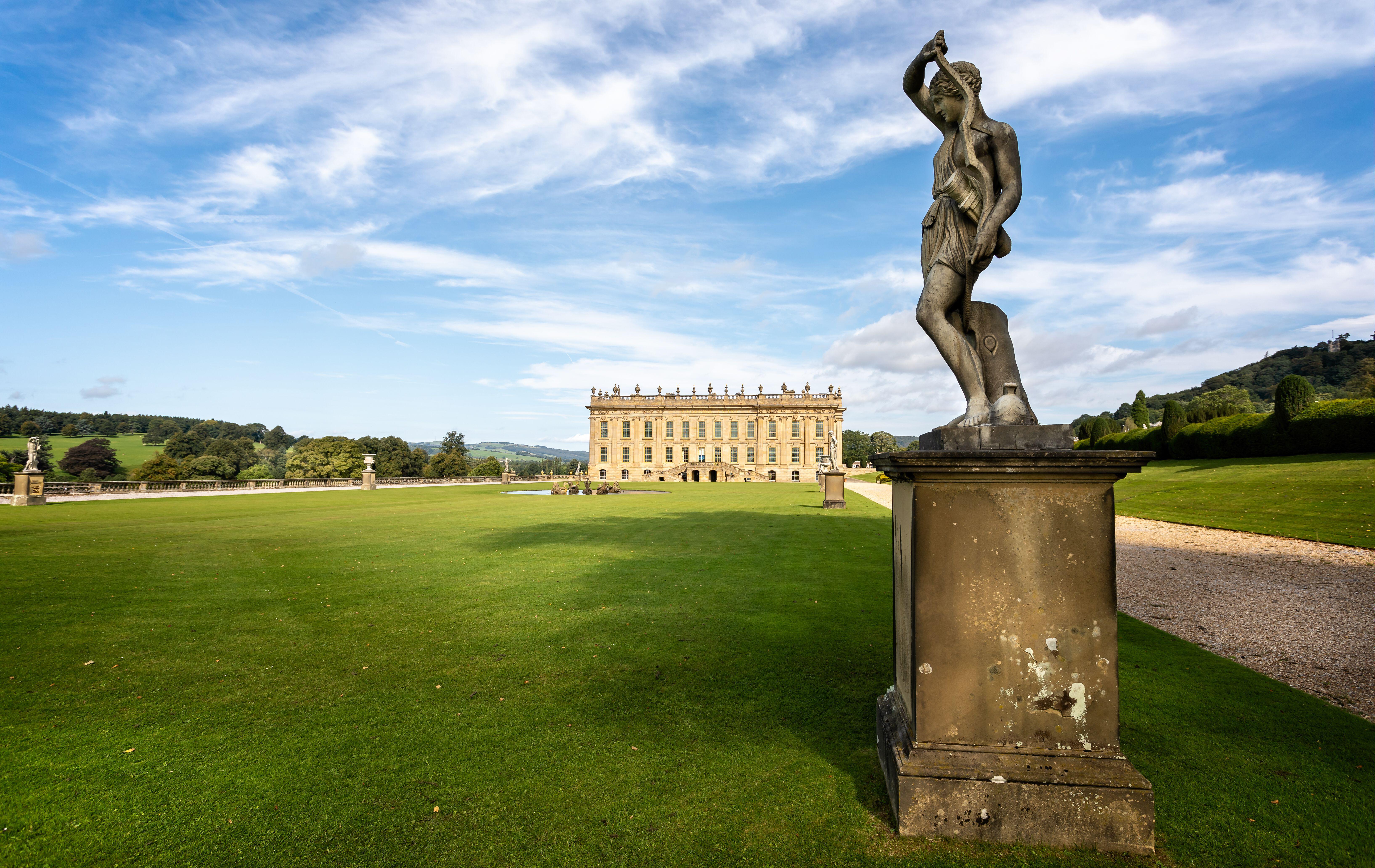 An ornate statue outside a magnificent mansion on flat green lawns