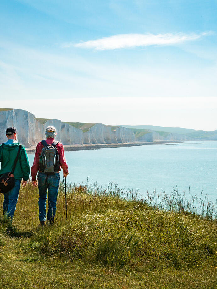 Two men hiking together with the stunning backdrop of white cliffs overlooking the ocean.
