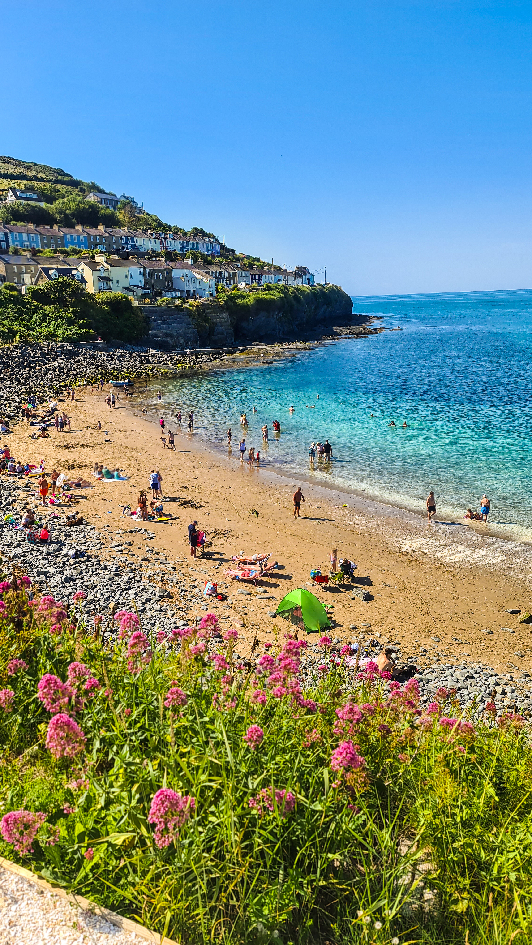 People on a sandy beach in a cove with houses on the cliff behind