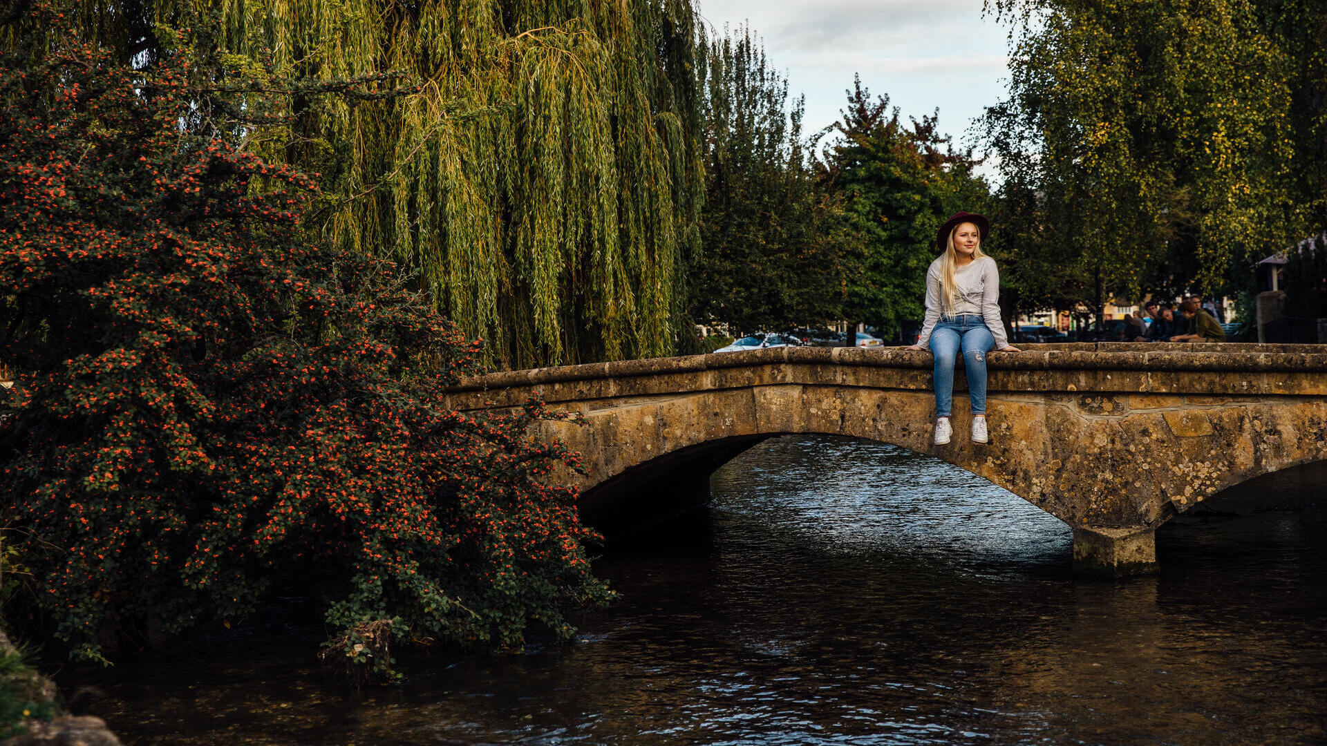 Woman sitting on low bridge over a river in a village