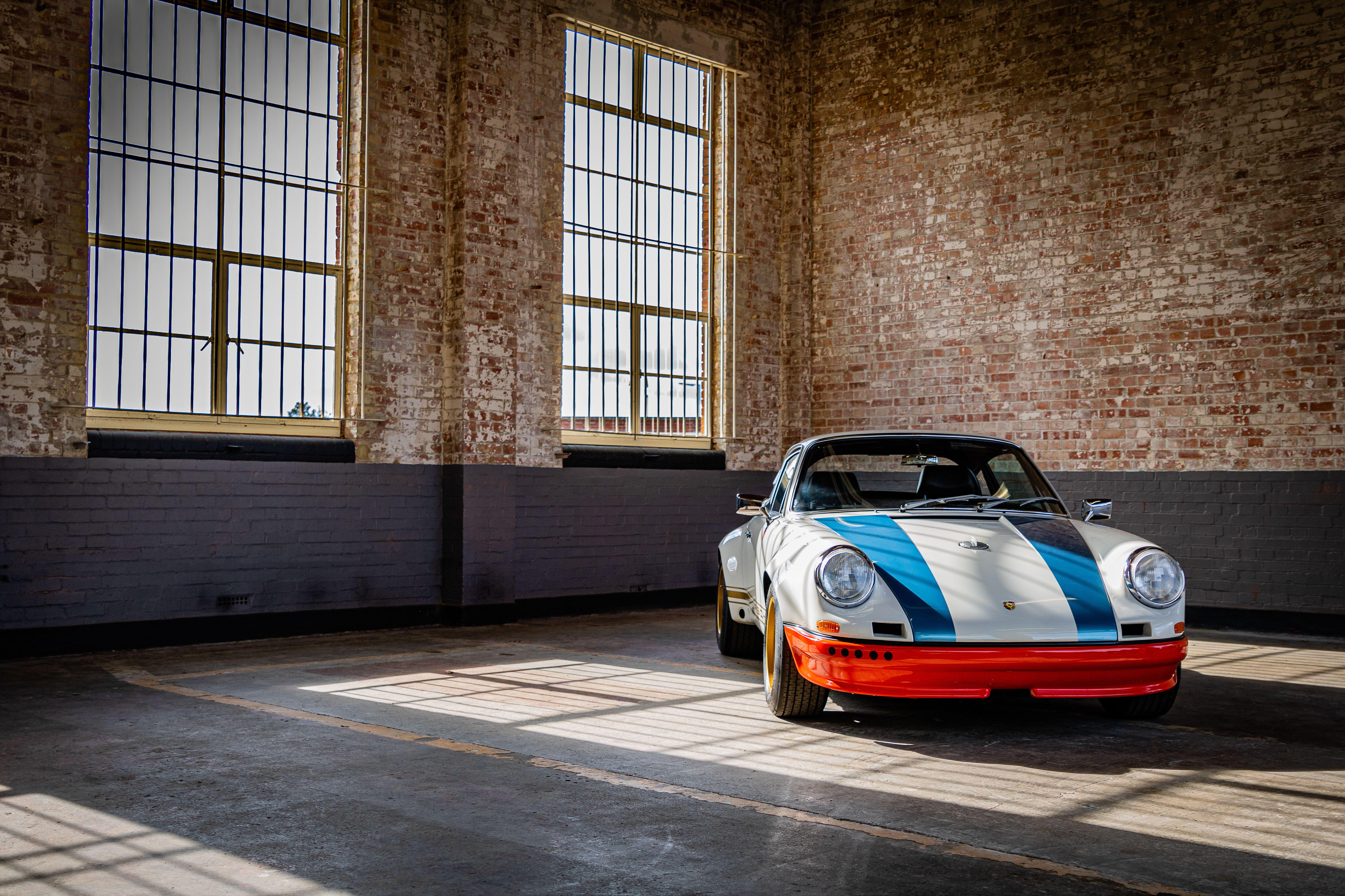 Classic race car with blue stripes and red bumper in an industrial space with brick walls and large windows.