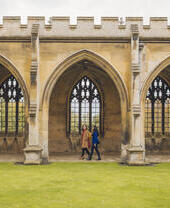 Two women walking under the arches of a college quad