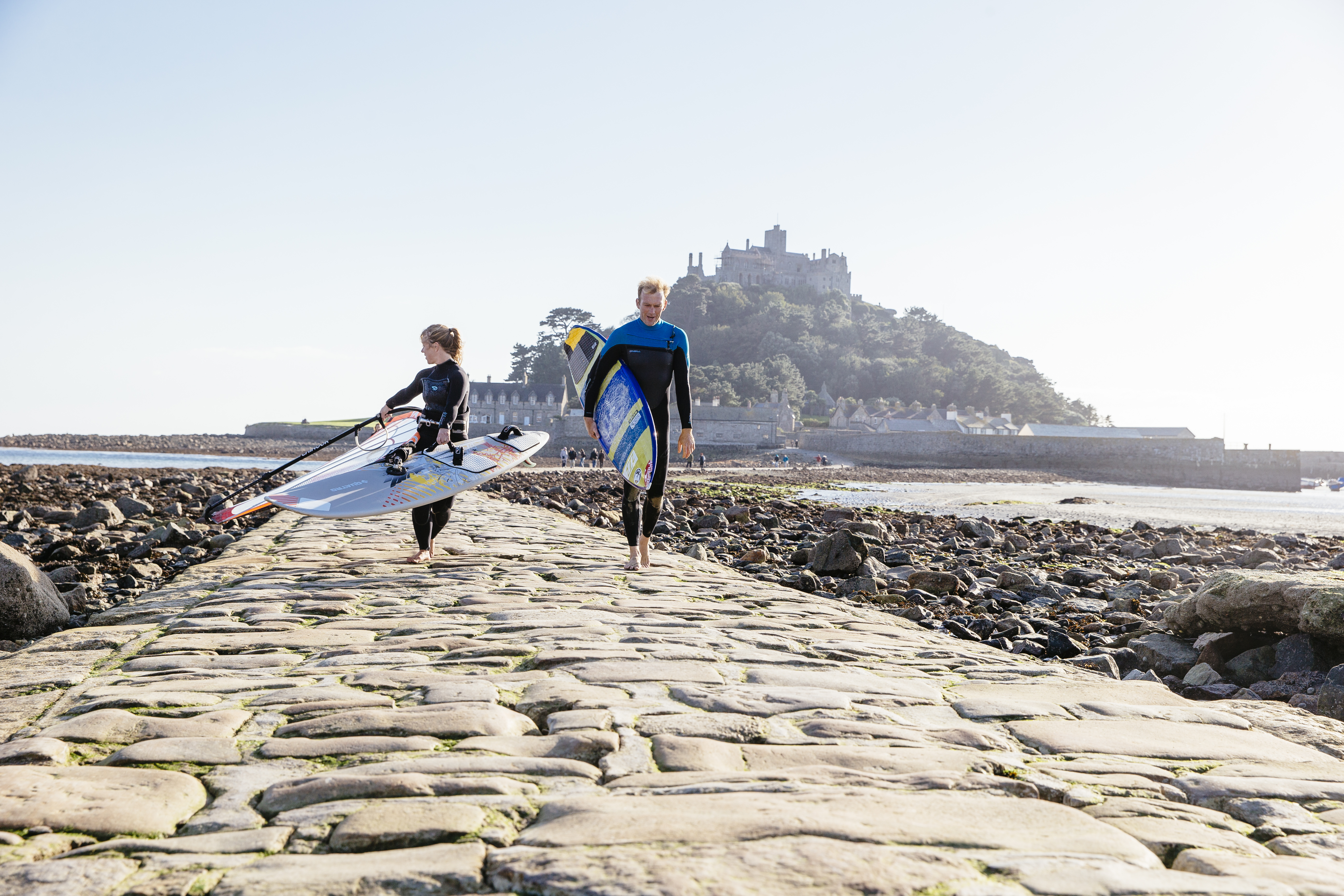 Windsurfers walking on a stone causeway that links an island to the mainland