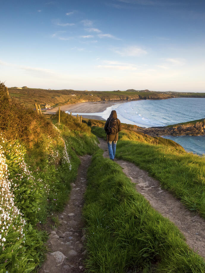 Randonneur traversant un sentier côtier surplombant une grande plage déserte.