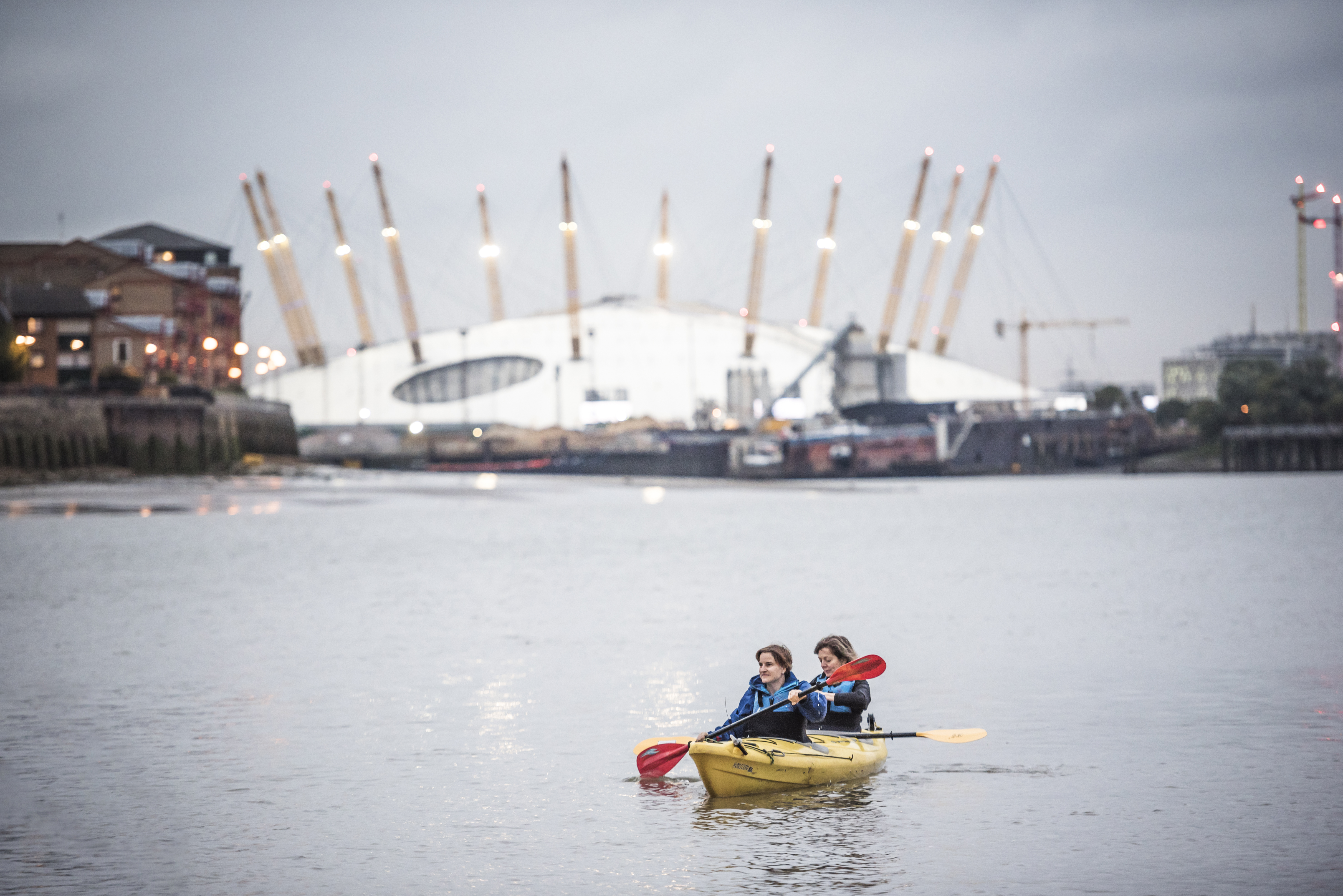 Two girls kayaking on the river in front of the O2 arena