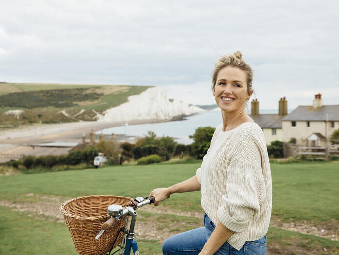 Lächelnde Frau auf einem Fahrrad mit weißen Klippen im Hintergrund
