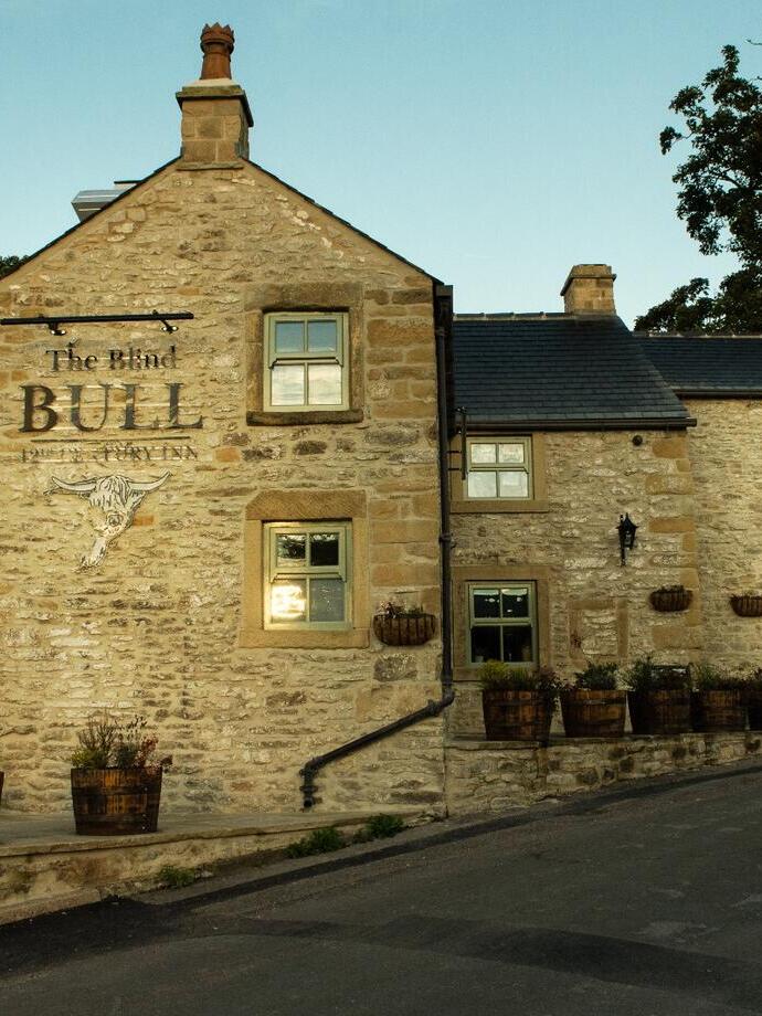 The sandy coloured stone building of a pub on the side of a road