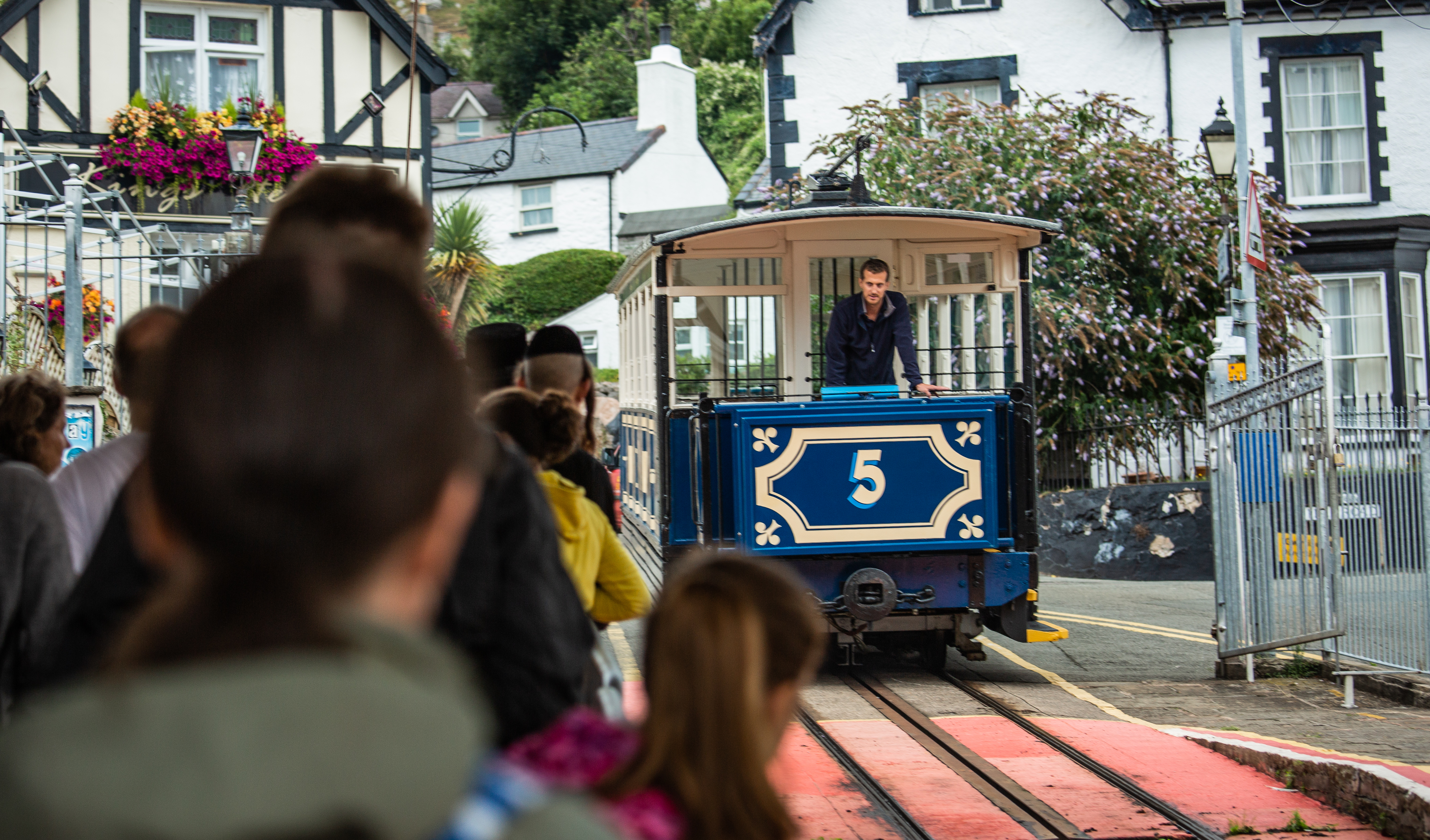 A line of people at a station queuing for a blue tram.