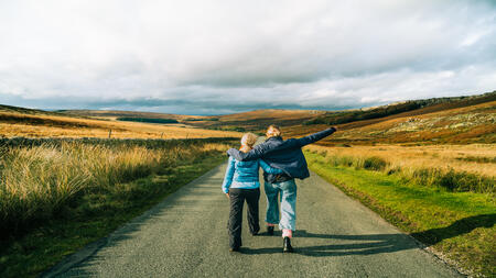 Rear view of two people walking down a countryside road