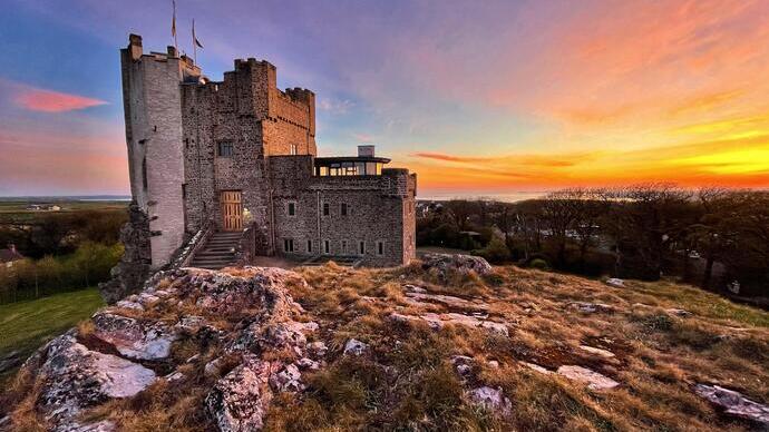 Château en pierre sur une colline au coucher du soleil avec ciel coloré.