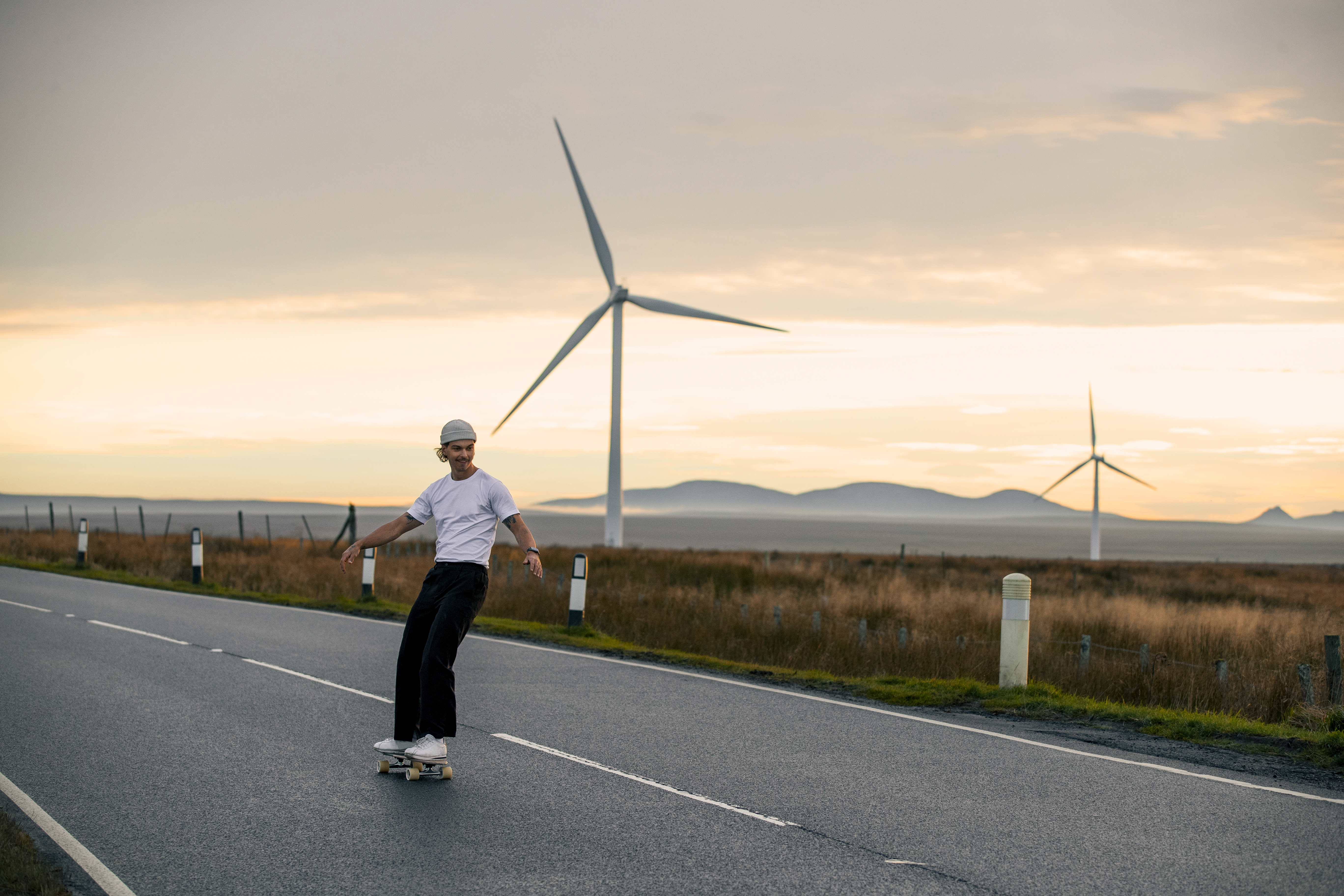 Man skateboarding on a road with wind turbines behind him