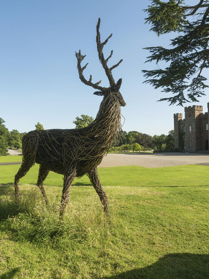 A wooden sculpture of a deer outside a castle.