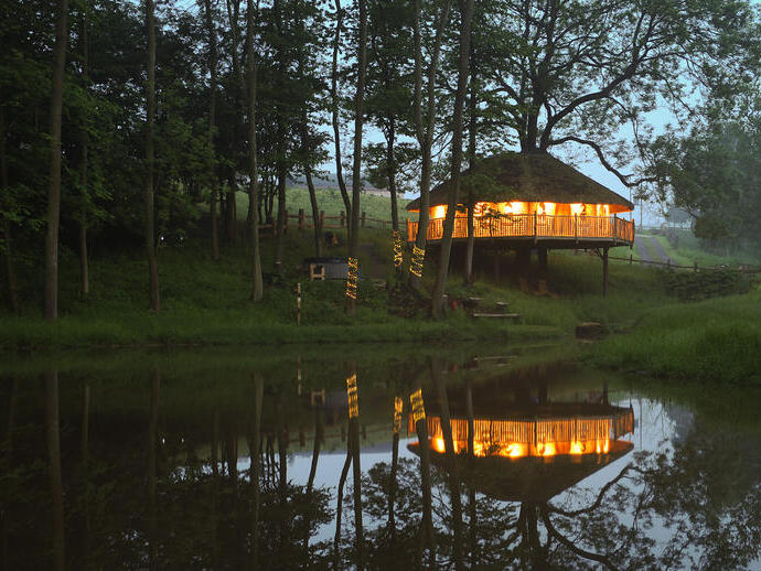 Overlooking the lake at dusk to the treehouse at Treeopia, light from within and surrounded by trees.