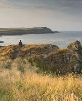 Persona caminando por un sendero costero con vistas a una bahía