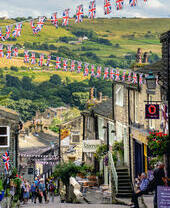 Gente caminando por una empinada calle empedrada de un pueblo con banderines de la Union Jack colgando de las casas