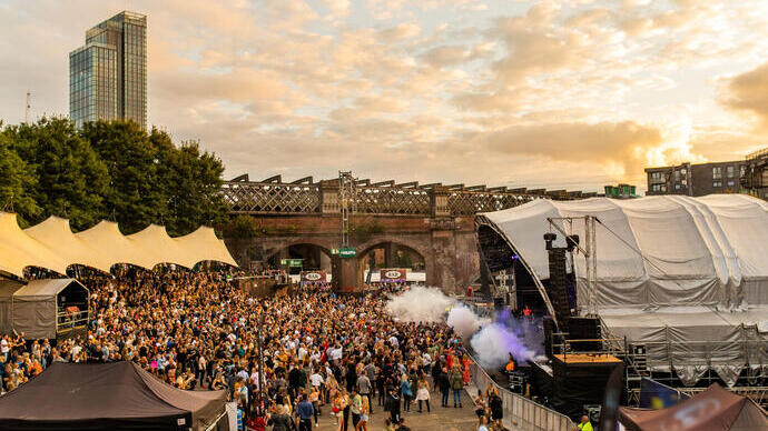 Crowds of people at a festival with stage on right in a city in evening light