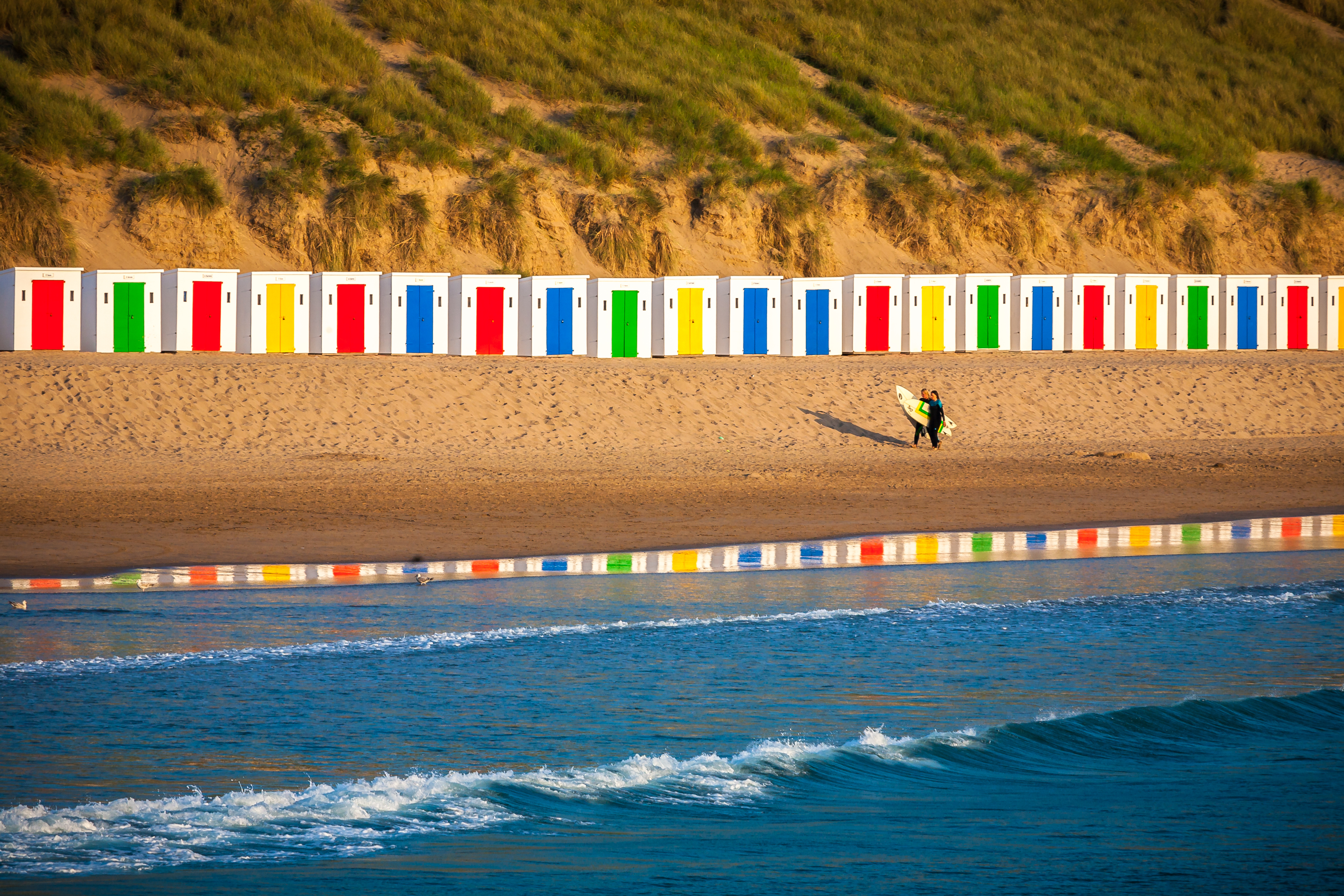 Idyllische Szene am Surferstrand mit schönen Strandhütten, die sich im Wasser spiegeln