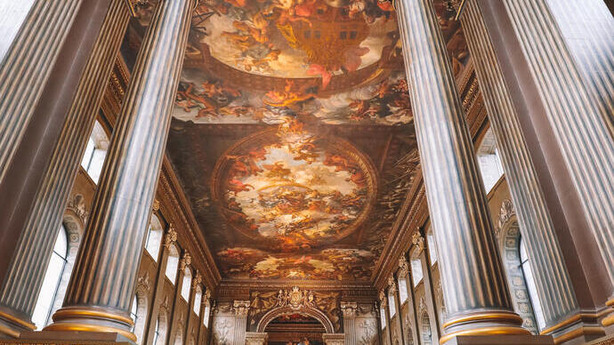 Man walking up a grand staircase towards a large hall with a painted ceiling