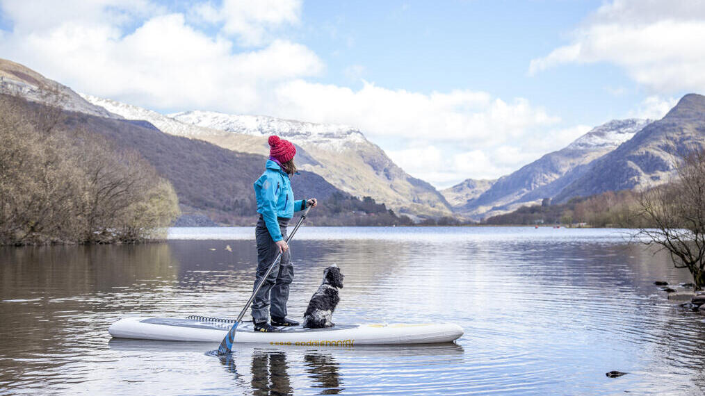 Woman and a dog on a paddleboard on a lake with mountains in the background