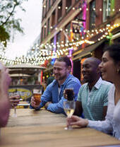 Friends having a drink sat at an outside table of a bar with fairy lights hanging behind