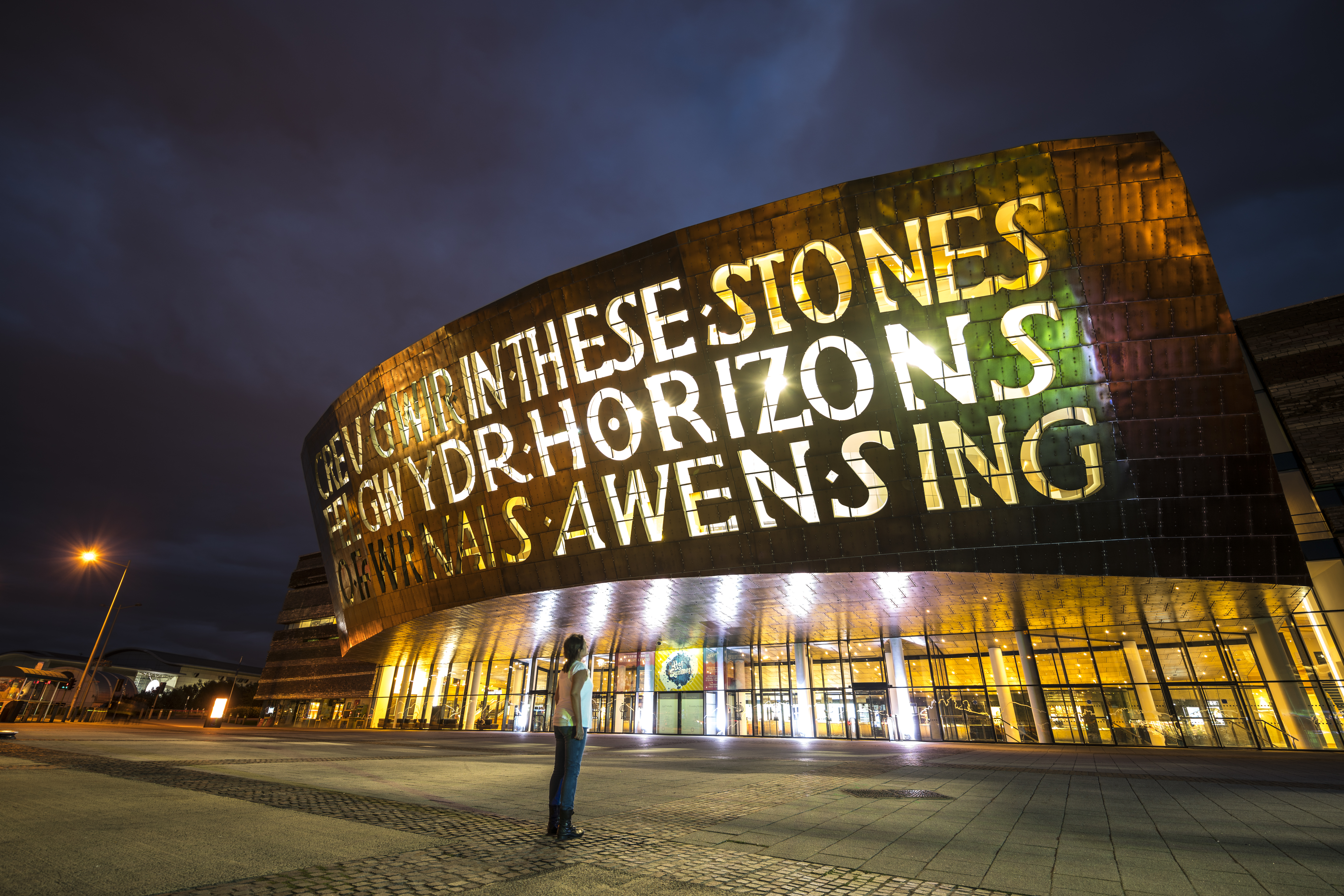 Person looking up at the front of a bronze building at night