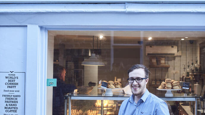 Mann, der vor einer Bäckerei ein Tablett mit Cornish Pasties hält