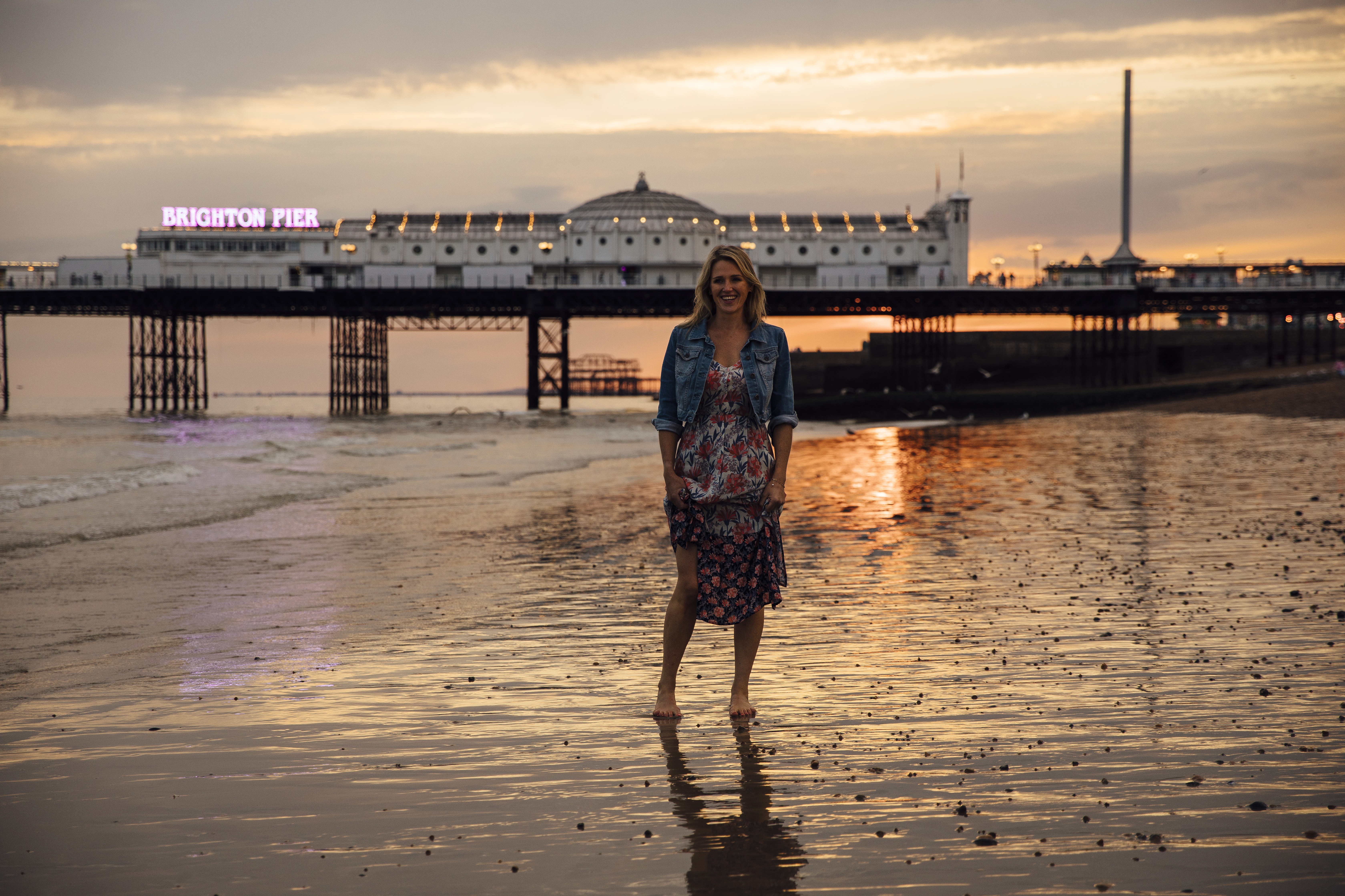 Donna in piedi sulla spiaggia vicino al molo al tramonto