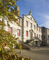 Extérieur d'une demeure seigneuriale en briques claires avec un escalier d'entrée, encadrée par la végétation.