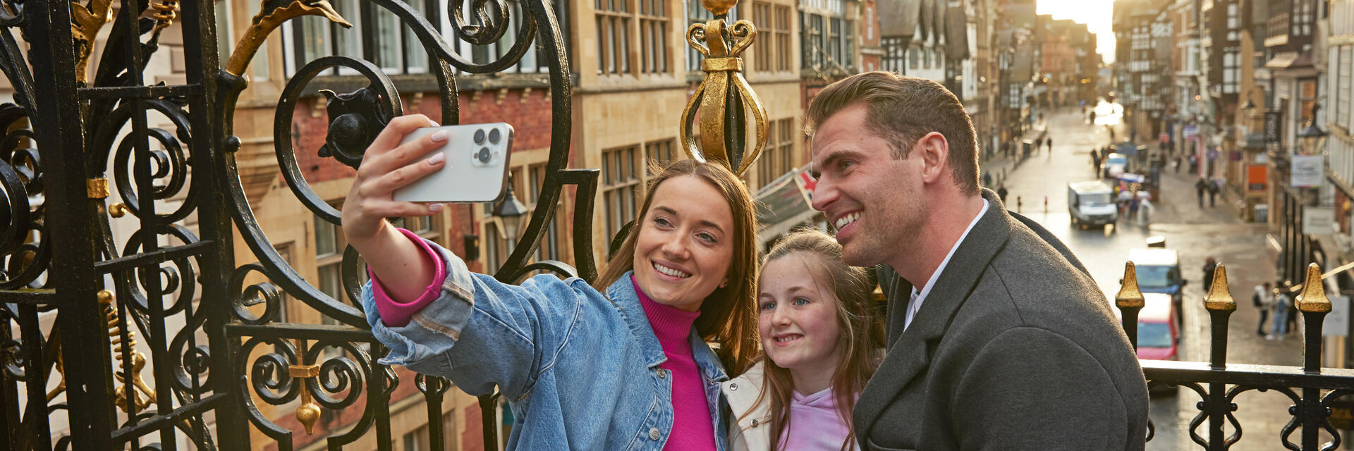 A family taking a selfie on a historic street with ornate ironwork and timber-framed buildings in the background.